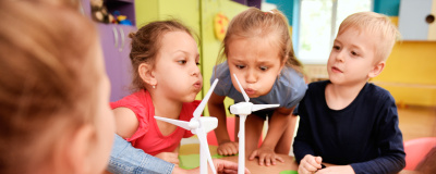 Einige Kindergartenkinder pusten auf ein Windrad-Modell
