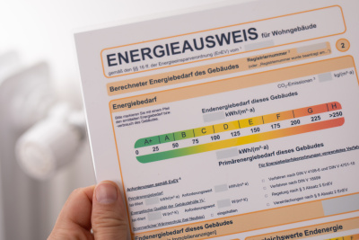 Eine Hand hält einen Energieausweis vor einer Heizung