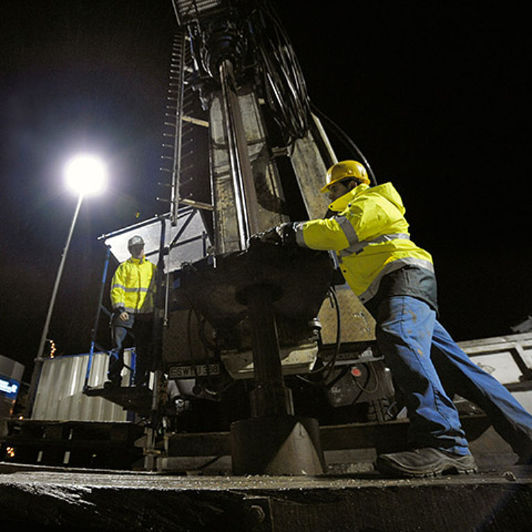 Zwei Bauarbeiter bedienen in der Dunkelheit ein Bohrgestänge